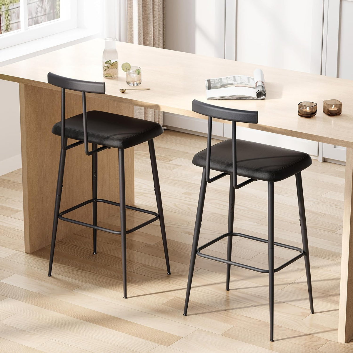 Pair of black PU leather counter-height stools angled front view beside a light wood counter in a bright room
