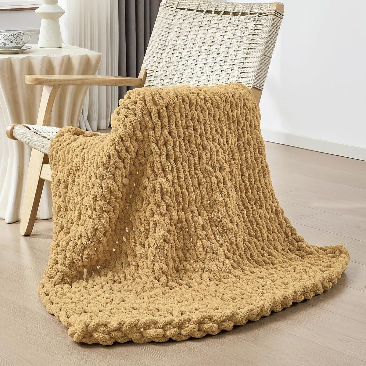 Warm camel-colored chunky knit blanket casually folded over the seat and arm of a woven rope-back chair.