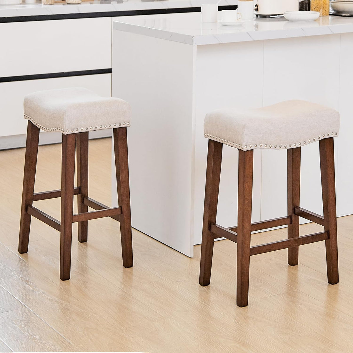 Pair of beige saddle stools beside a white kitchen island on light wood flooring, angled front view