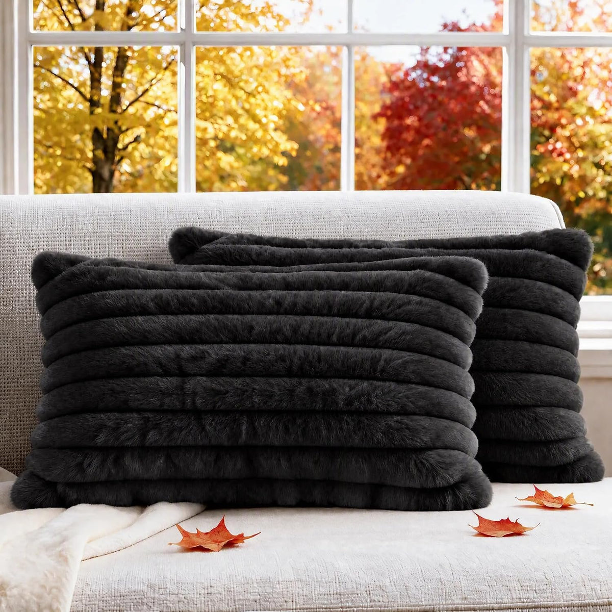 Pair of dark charcoal faux fur ribbed pillow covers arranged on a pale couch with fall foliage outside
