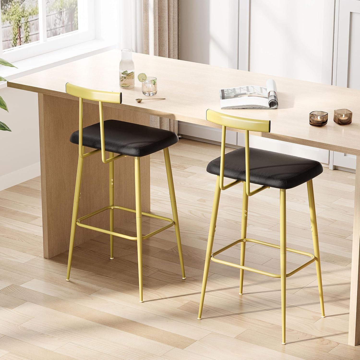 Two tall yellow metal bar stools with black cushioned seats tucked under a light wood counter in a bright room