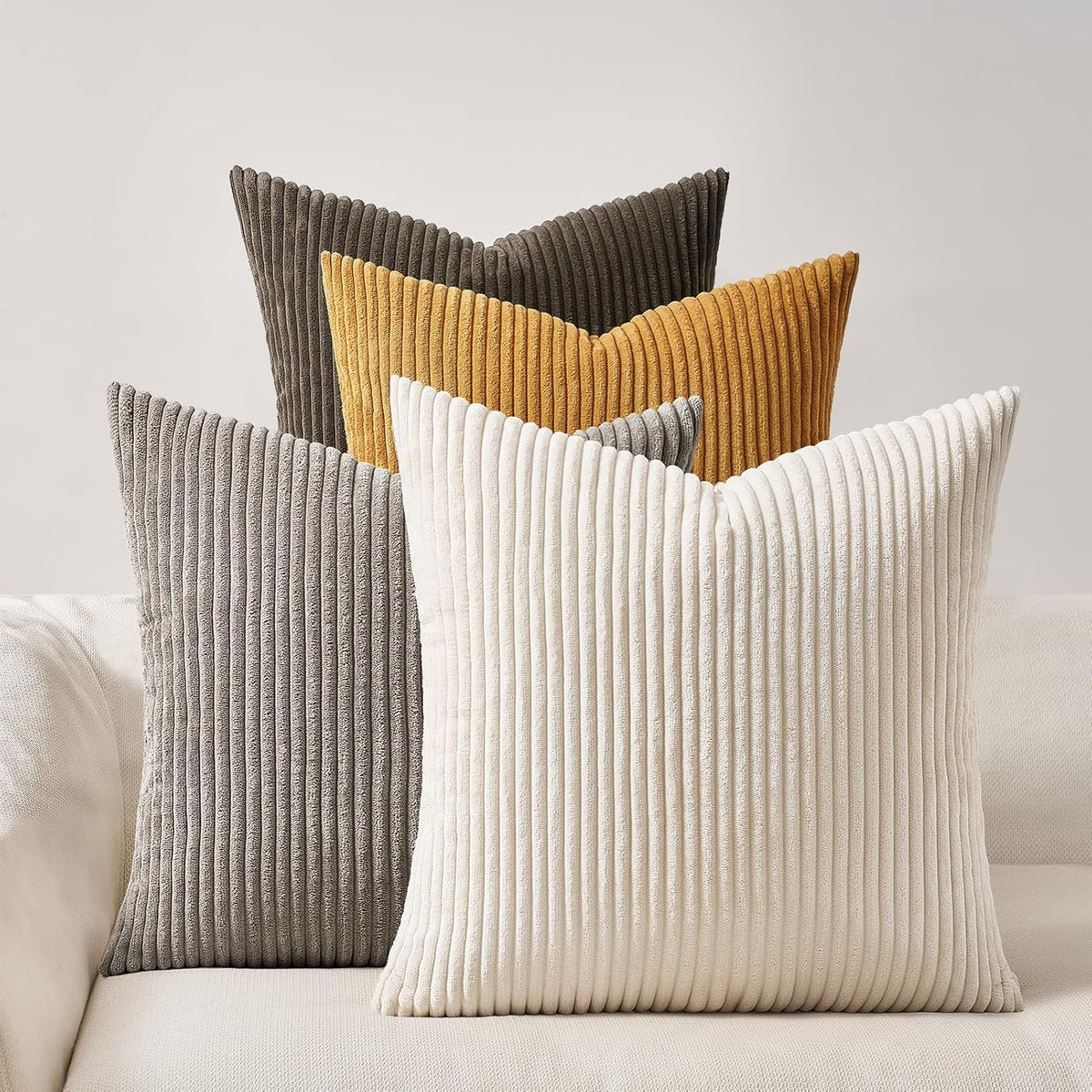 Three ribbed square pillows in gray, cream and mustard layered on a neutral couch.