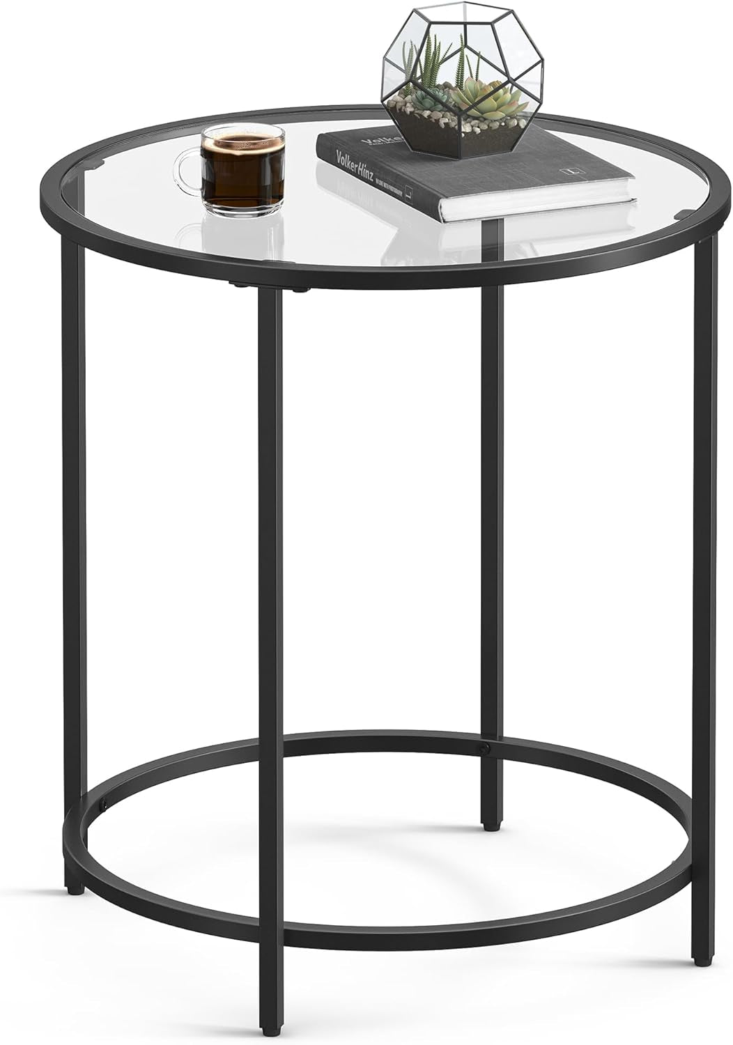 Black round side table with a clear glass top holding a book, small terrarium and a coffee cup.