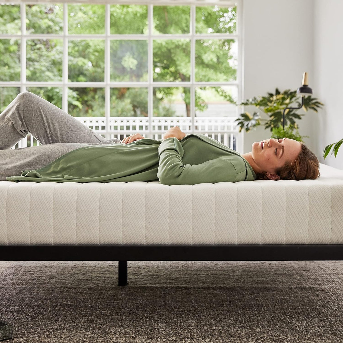 Side view of a person lying on the mattress in a sunny room showing the mattress profile and support.