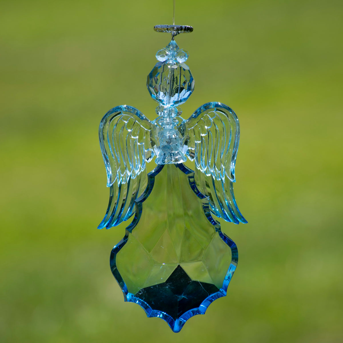 Blue faceted angel ornament hanging against a soft green background, with wings angled downward.
