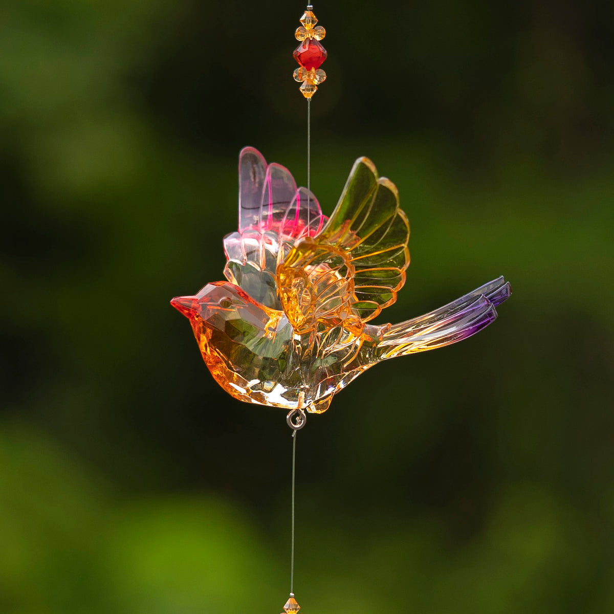 Translucent multicolored acrylic bird ornament with raised wings and bead accents, suspended against a dark green background.