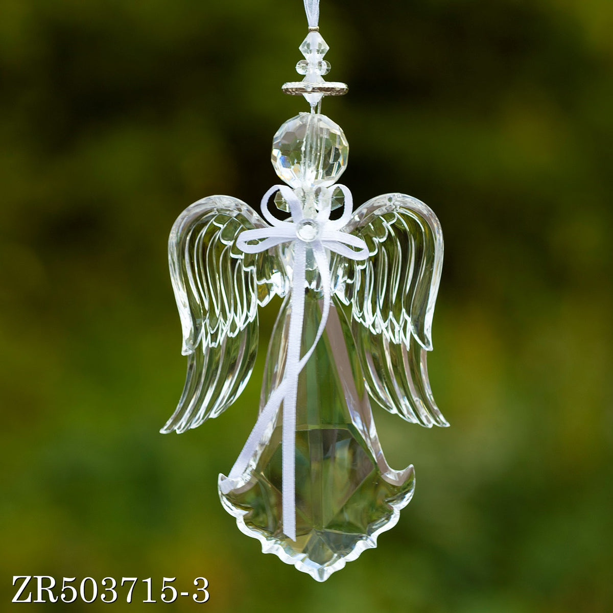 A clear angel ornament hangs upright, showing layered wings and a ribbon bow against a blurred green backdrop.