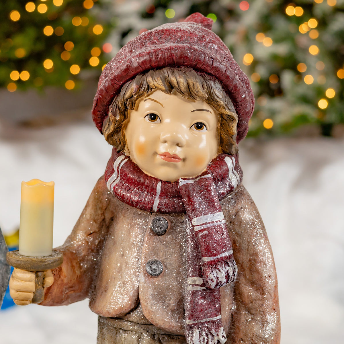 Close-up of a child figure in a red hat and scarf holding a candle.
