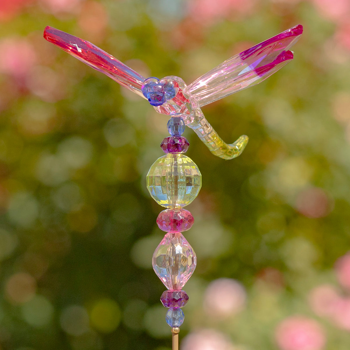 Translucent dragonfly with pink and purple wings perched above multicolored faceted beads.