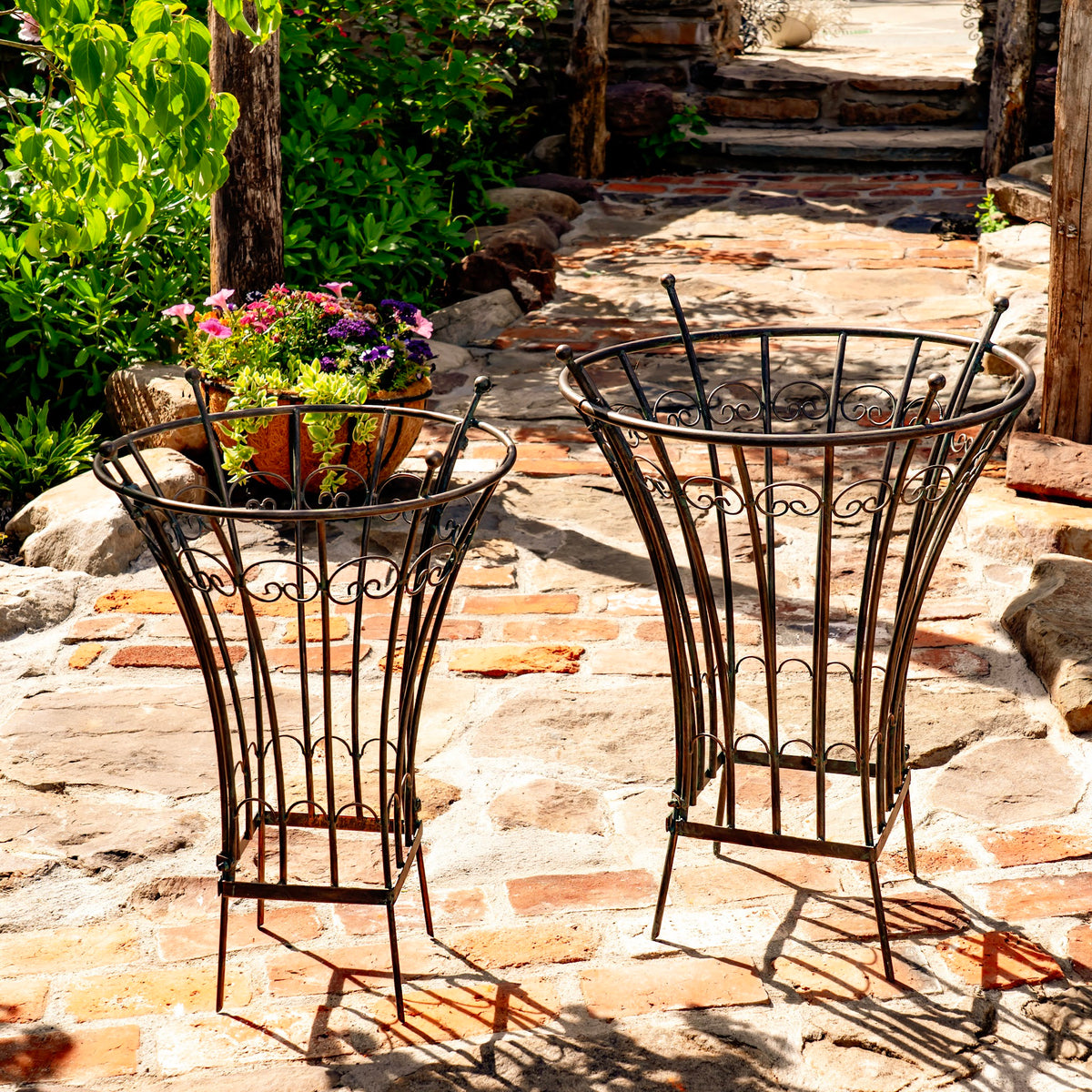 Matching openwork garden stands shown together on a sunlit brick and stone walkway.