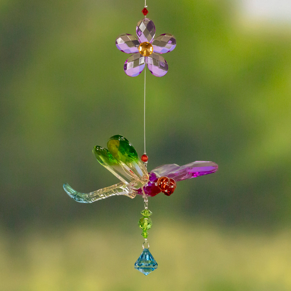 A multicolored faceted dragonfly ornament hangs beneath a purple flower, with beads and a blue drop.