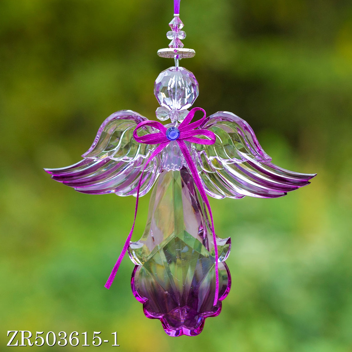 A purple-accented clear angel hangs from a beaded loop, its wings extending horizontally against a soft green background.