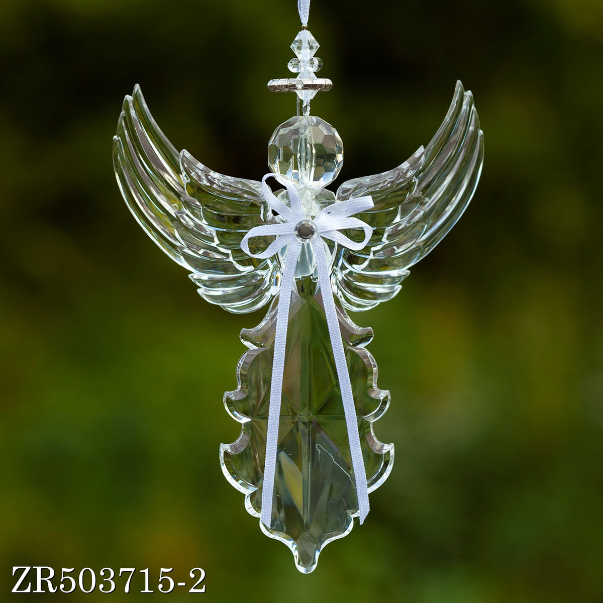 An upward-winged clear angel ornament hangs against green, with a white bow at its center.
