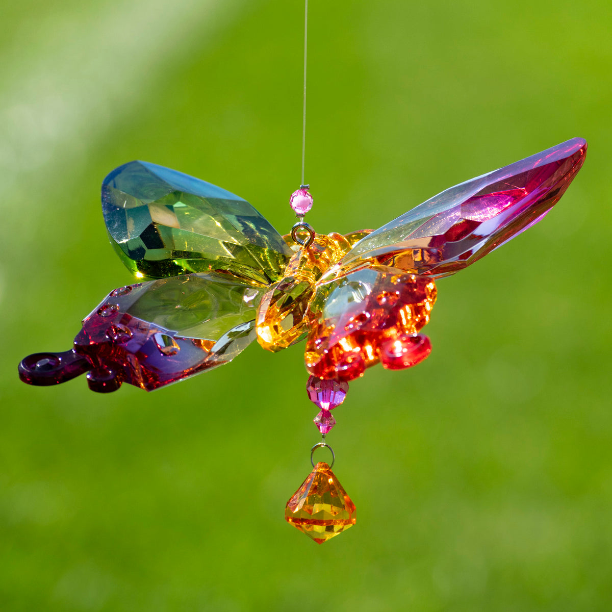 Angled view of a multicolored acrylic butterfly ornament with a small jewel hanging beneath it.