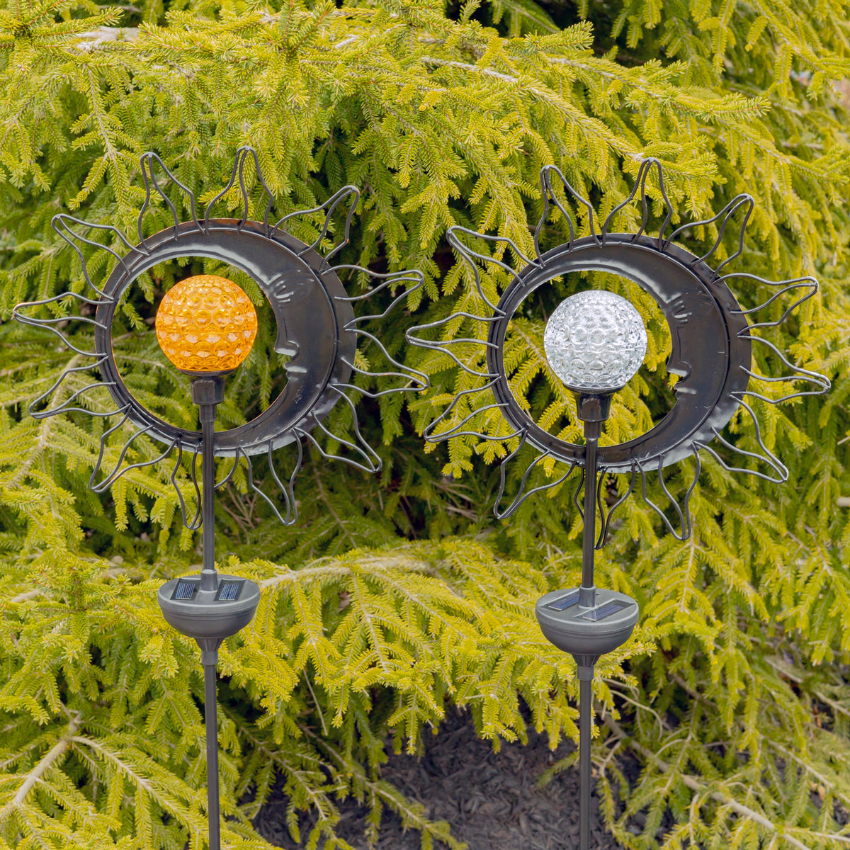 Two garden stakes shown from behind, with amber and clear globes against evergreen branches.