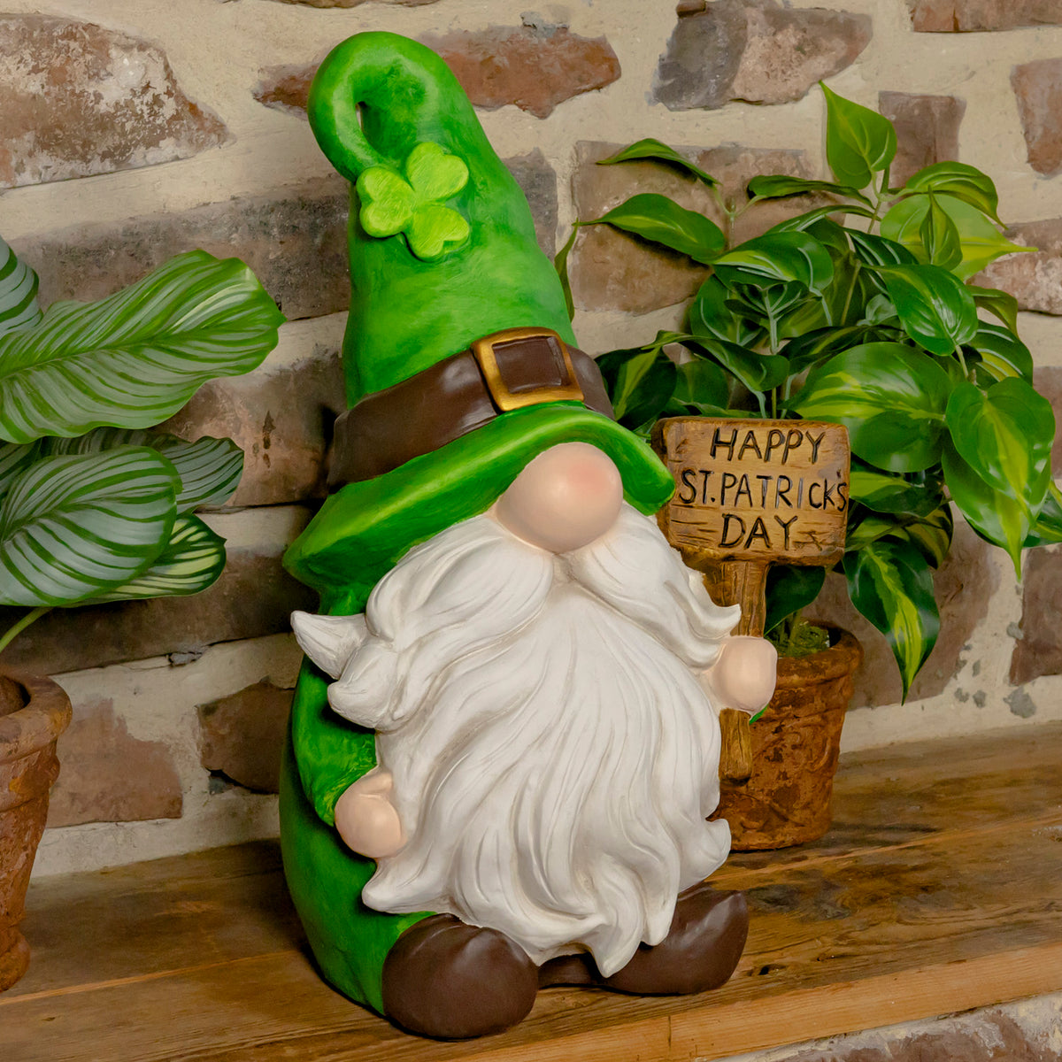 Green-hatted garden gnome with a white beard holds a small wooden sign beside potted plants.