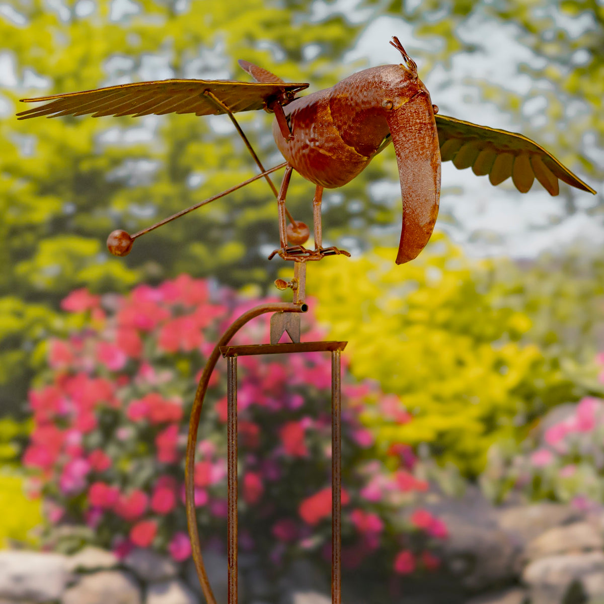 Rust-colored metal toucan with outstretched wings on a garden stake among flowers