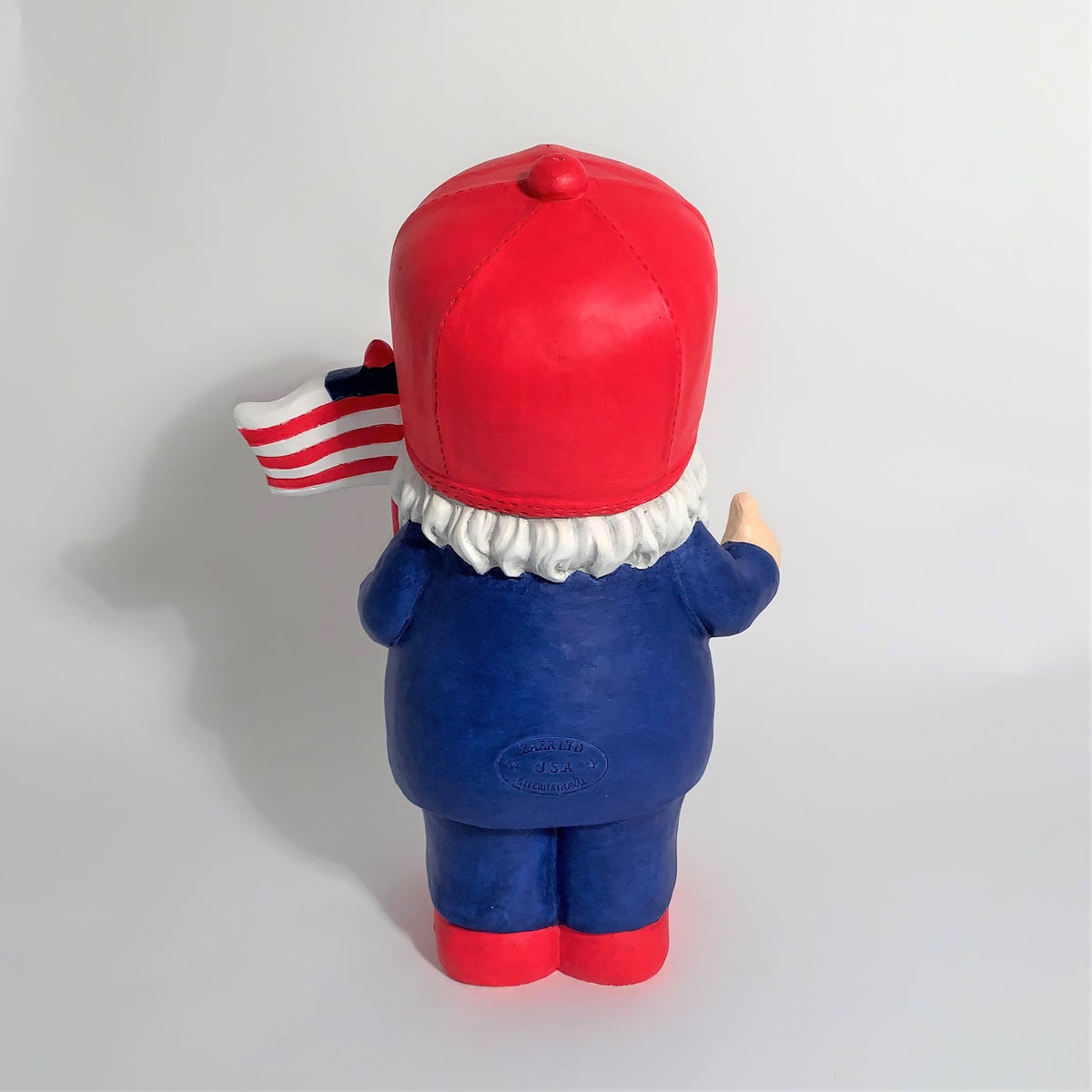 Back view of a red-hatted, blue-clothed garden gnome with a flag