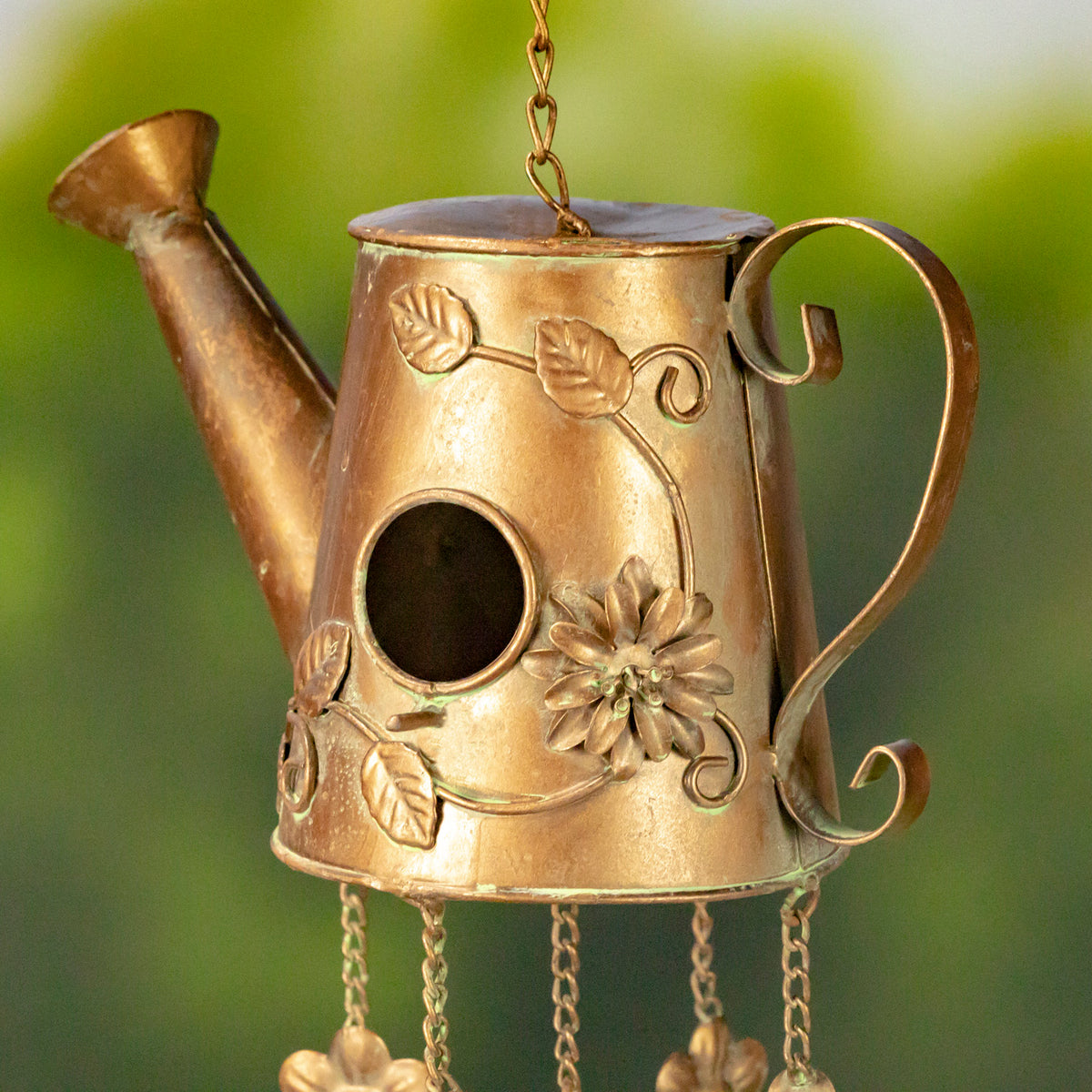 Close-up of the watering-can birdhouse, showing its round opening, raised floral details, curved handle and spout.