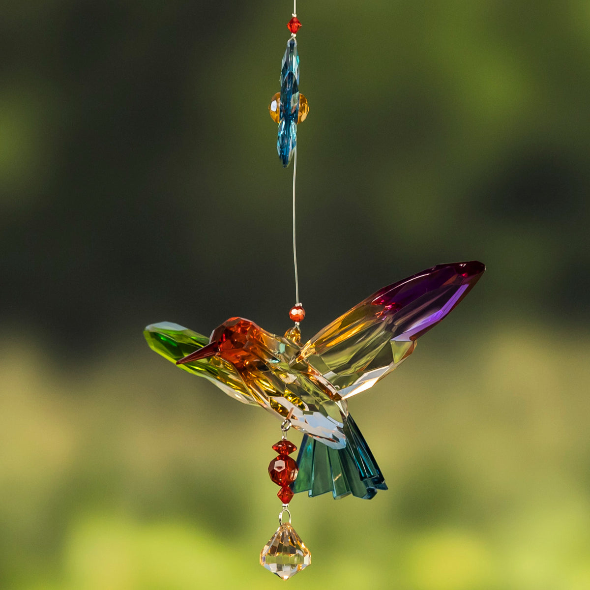 A multicolored faceted hummingbird seen from the side hangs below a narrow blue ornament.