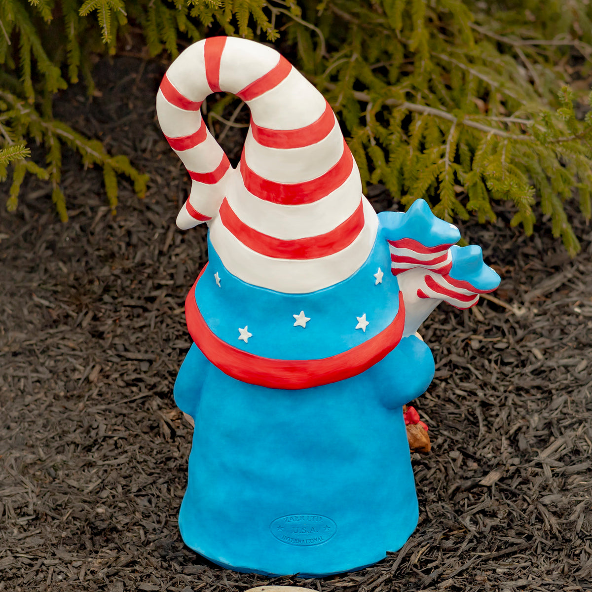 Back view of a blue garden gnome with a red-and-white striped hat outdoors