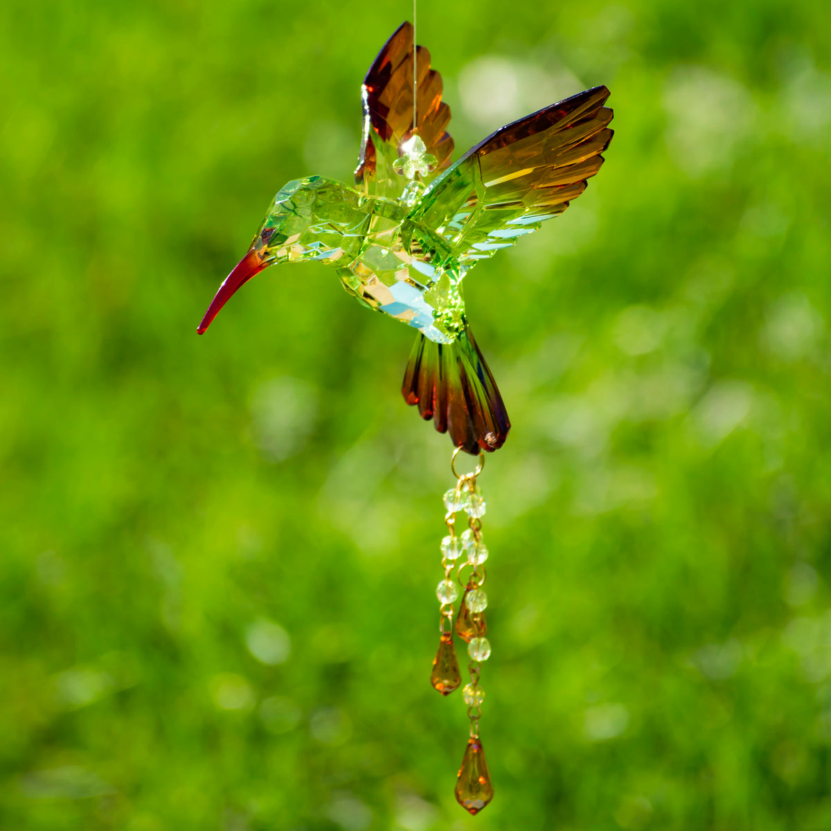 Amber and green faceted hummingbird ornament with clear beads and amber drops against a blurred green background.