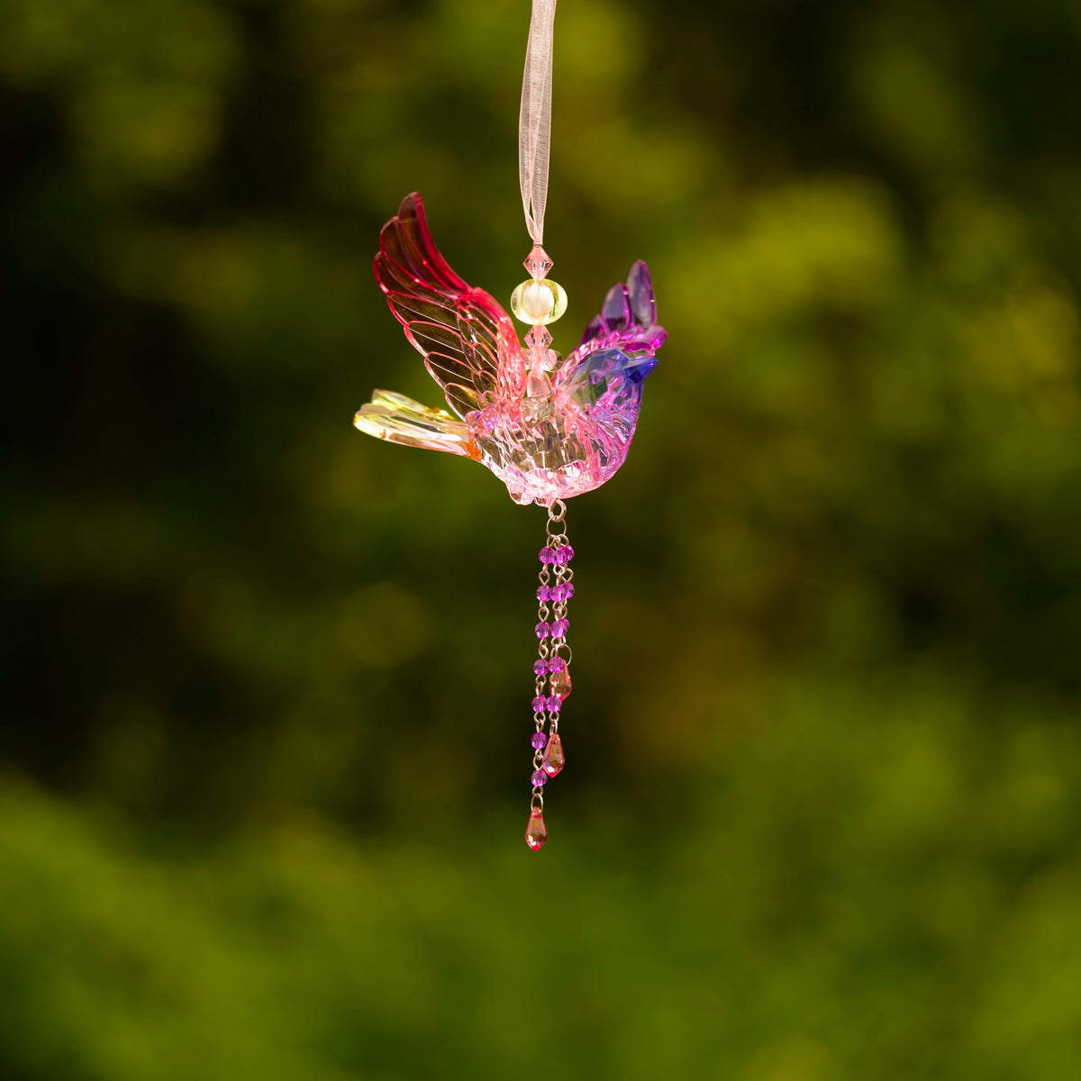 Pink and purple translucent bird ornament suspended from a pale ribbon, with dangling decorative beads.