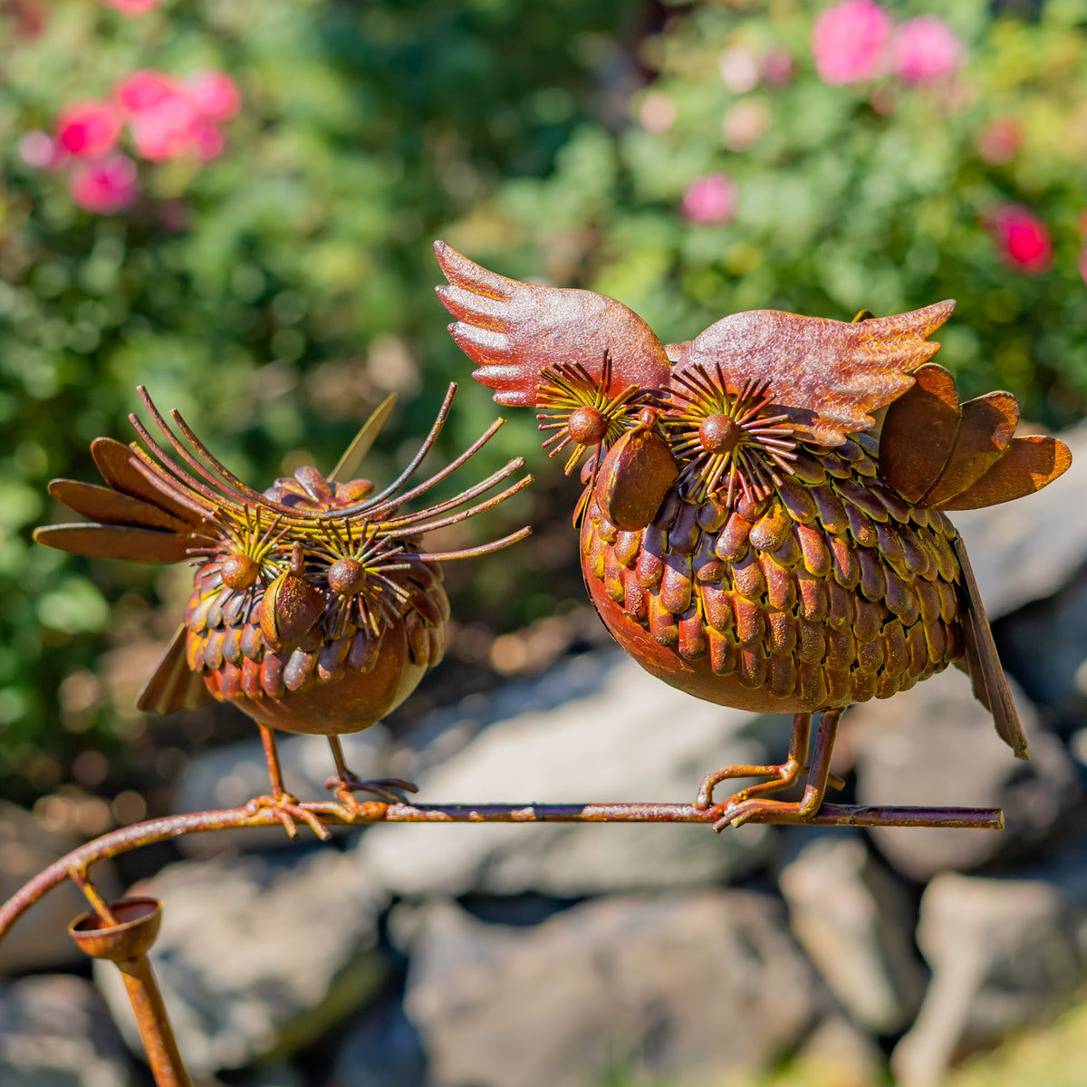 Close view of two metal birds with layered feather details perched on a garden stake outdoors.