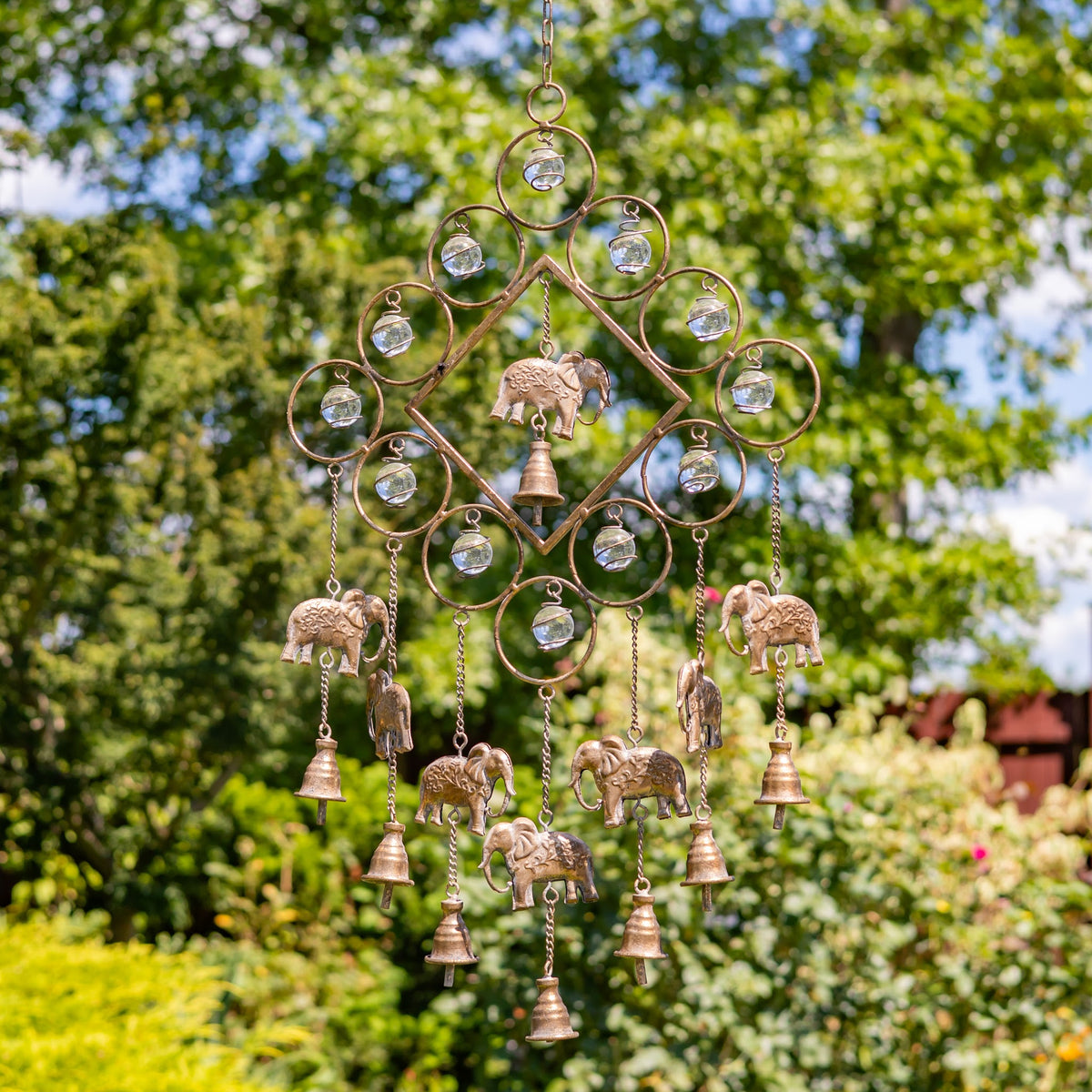 Metal wind chime with circular accents, hanging elephant ornaments, and small bells against a leafy garden.