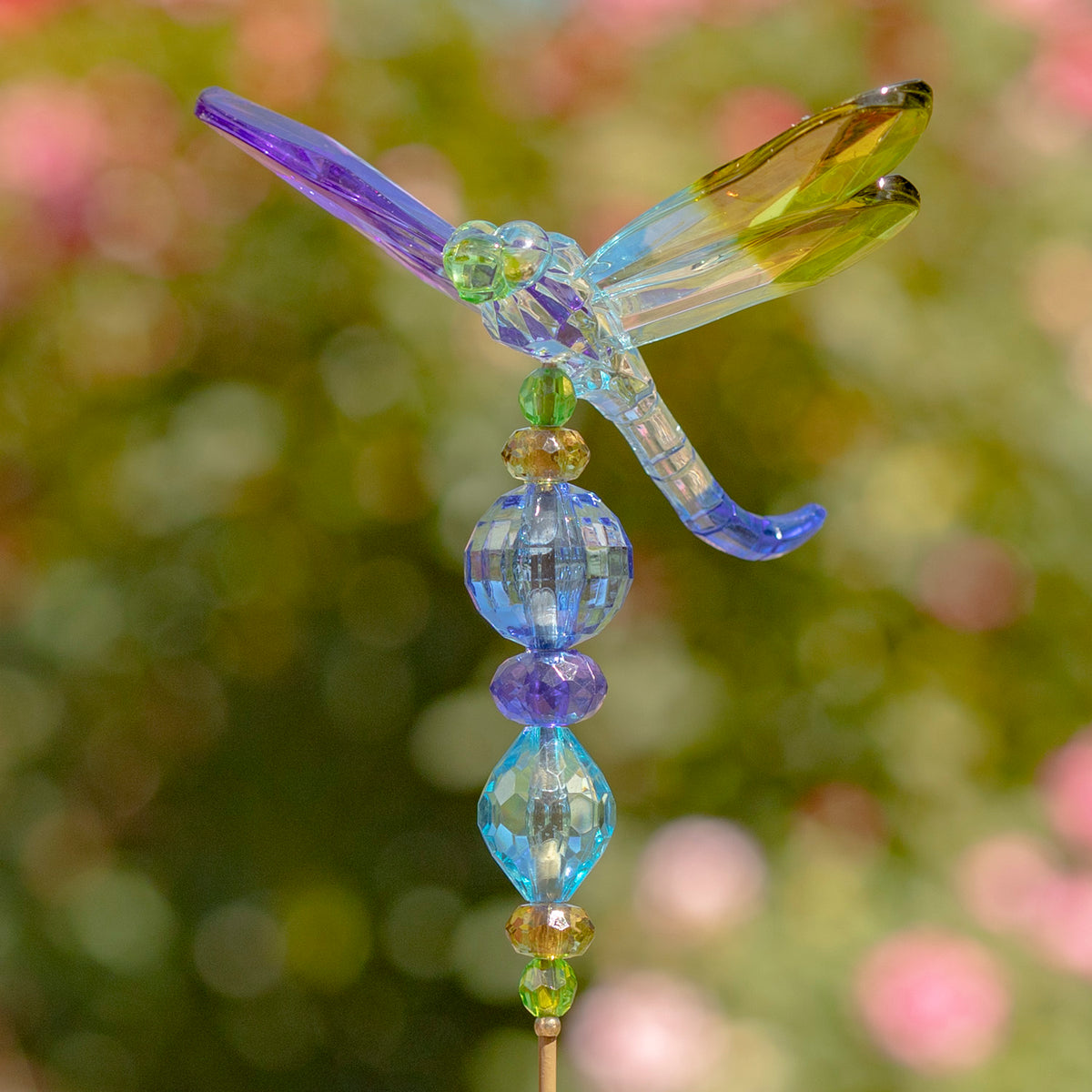 Blue, purple, and yellow-green dragonfly with spread wings above a column of colorful faceted beads.