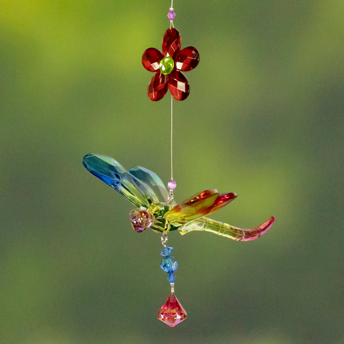 A multicolored dragonfly ornament with a red flower and dangling blue and pink beads hangs against green.