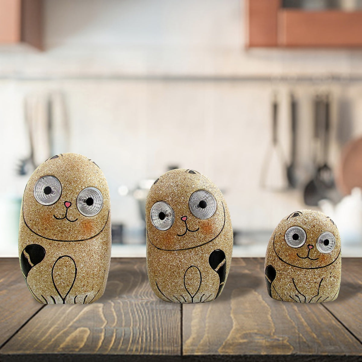 Three speckled cat ornaments in different sizes lined up on a wooden table.