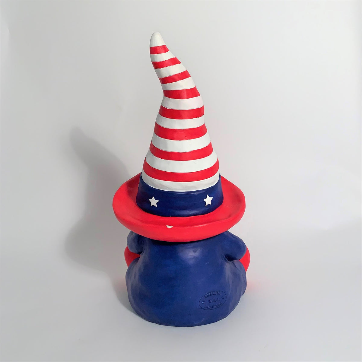 Back view of a seated garden gnome with a red, white and blue striped hat