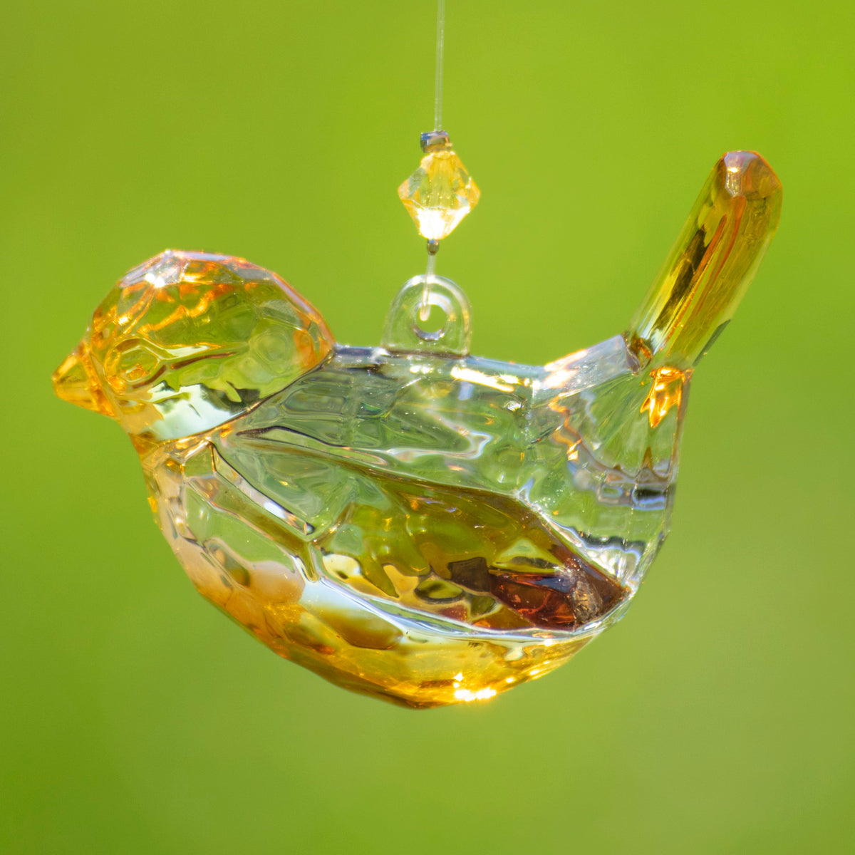 An amber-colored faceted bird ornament hangs in profile against a bright green background.