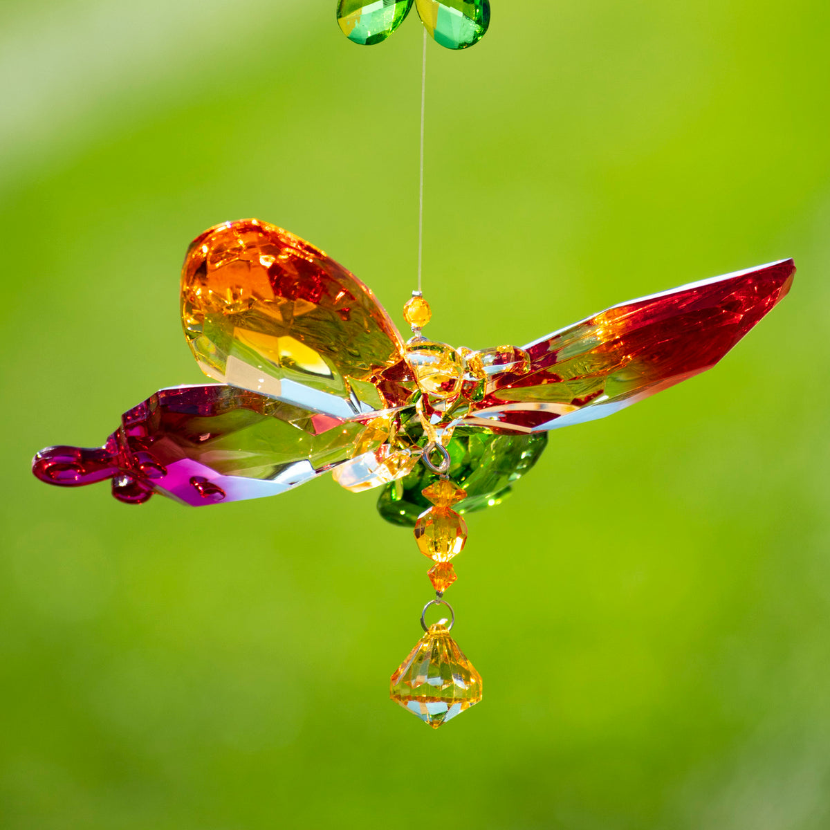 Close-up of an orange, red, and green faceted butterfly ornament suspended beneath a small flower.