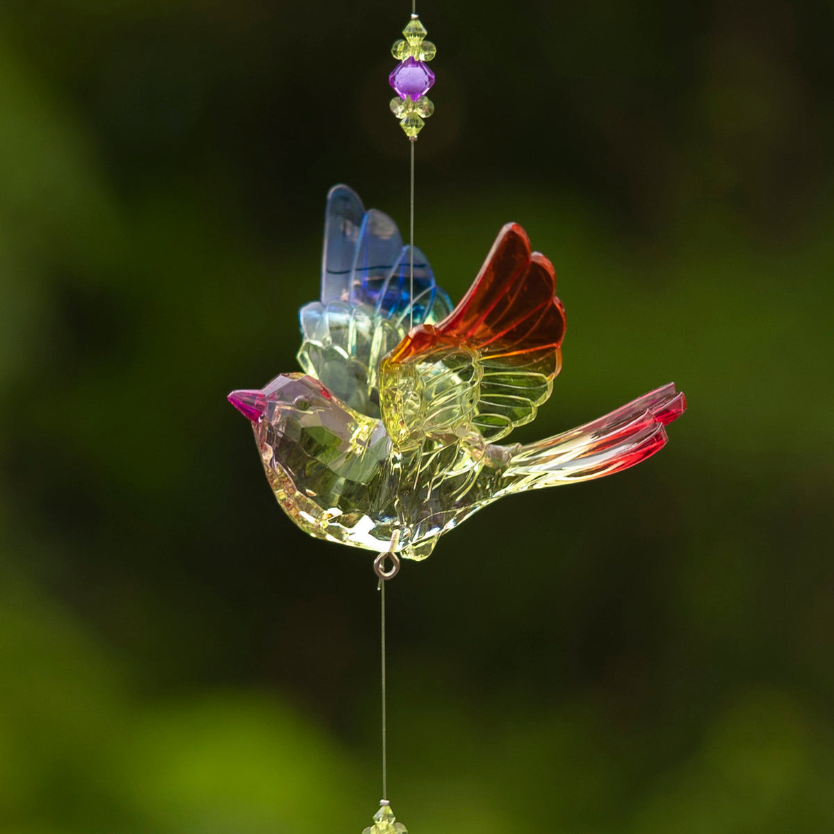Close view of a clear bird ornament with blue, red, and purple accents and beads on its hanging string.
