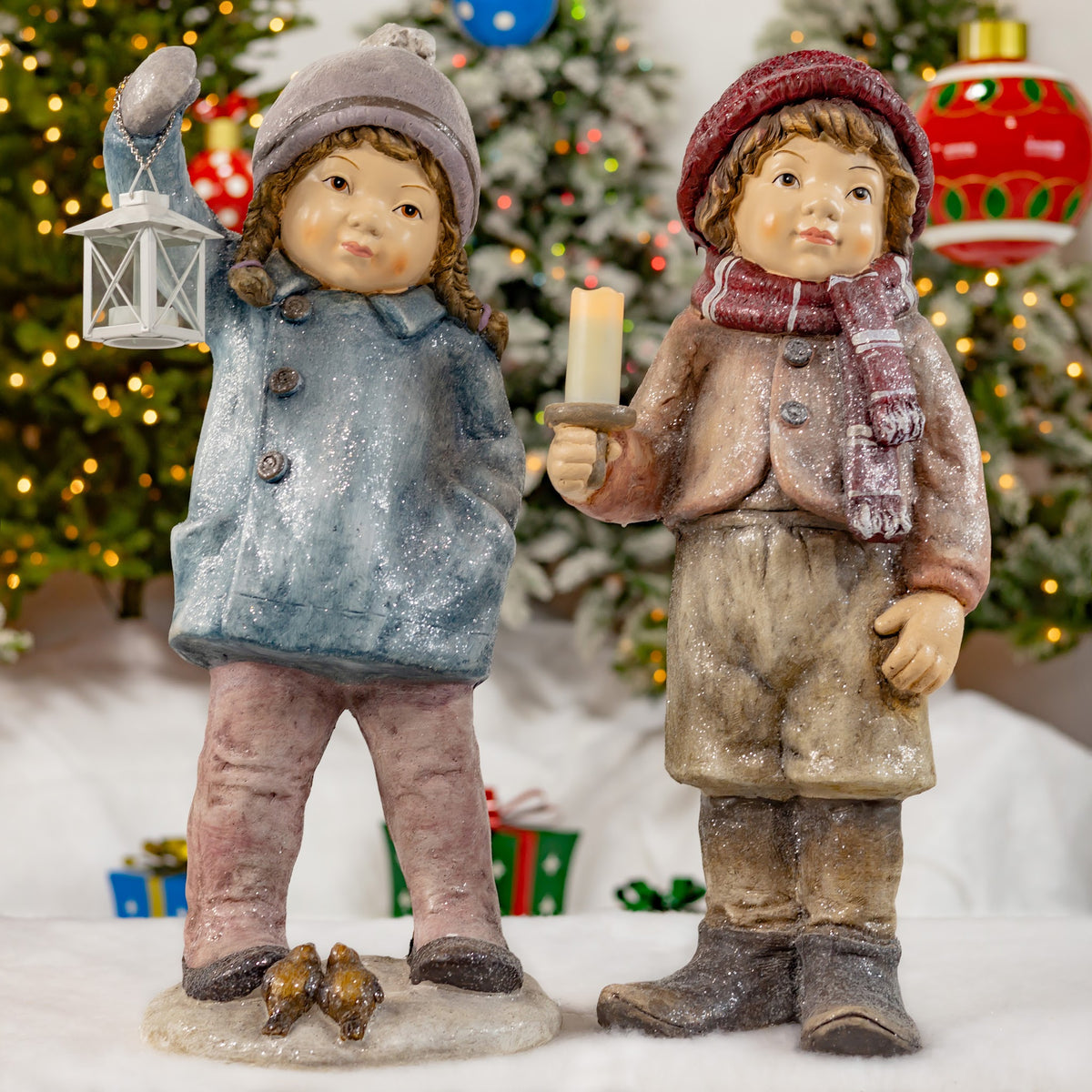 Two winter-clothed child figures stand together, one holding a lantern and the other a candle.