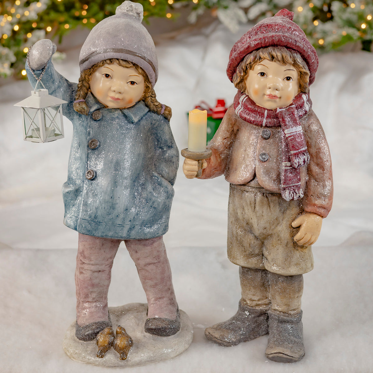 Boy and girl Christmas figurines with lantern and candle holder in a snowy setting
