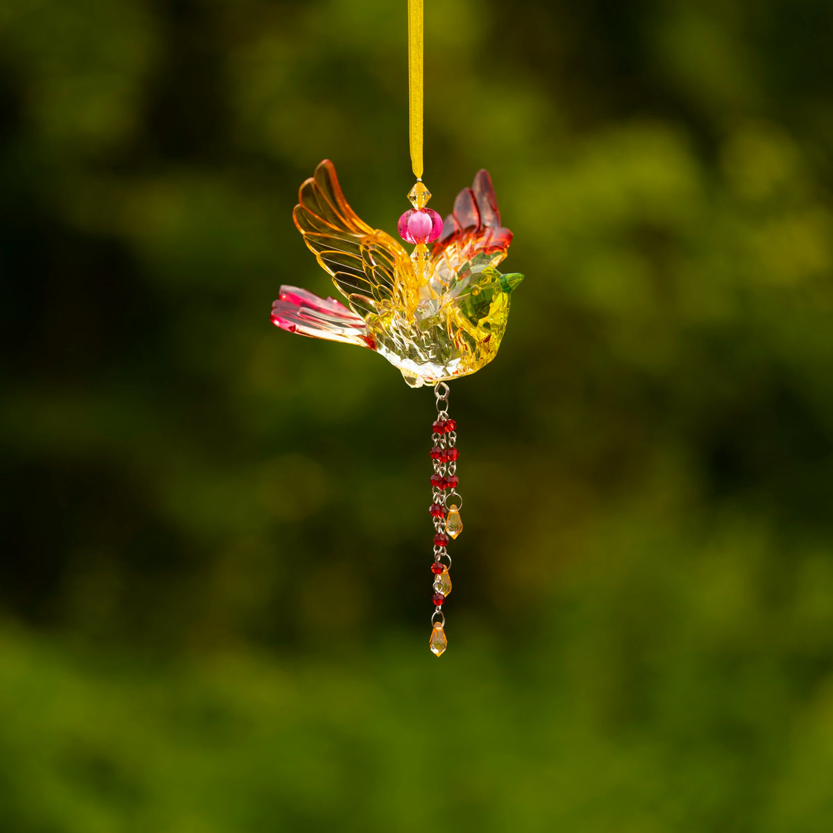 Back view of a multicolored bird ornament hanging by a yellow ribbon with beads dangling below.