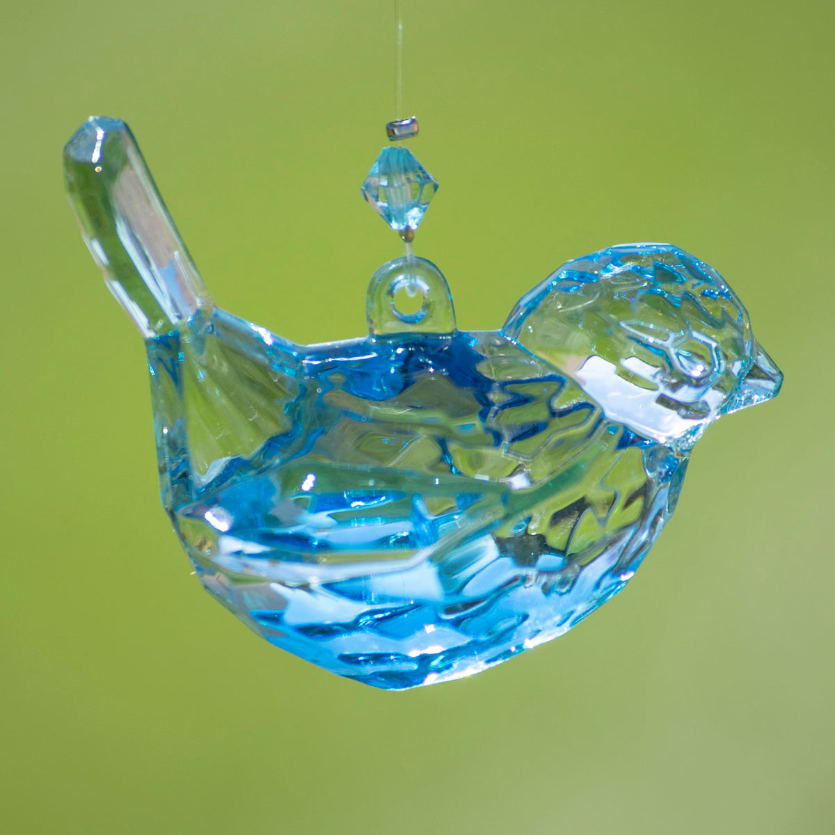 Faceted clear bird ornament with bright blue reflections, hanging against a lime-green background.