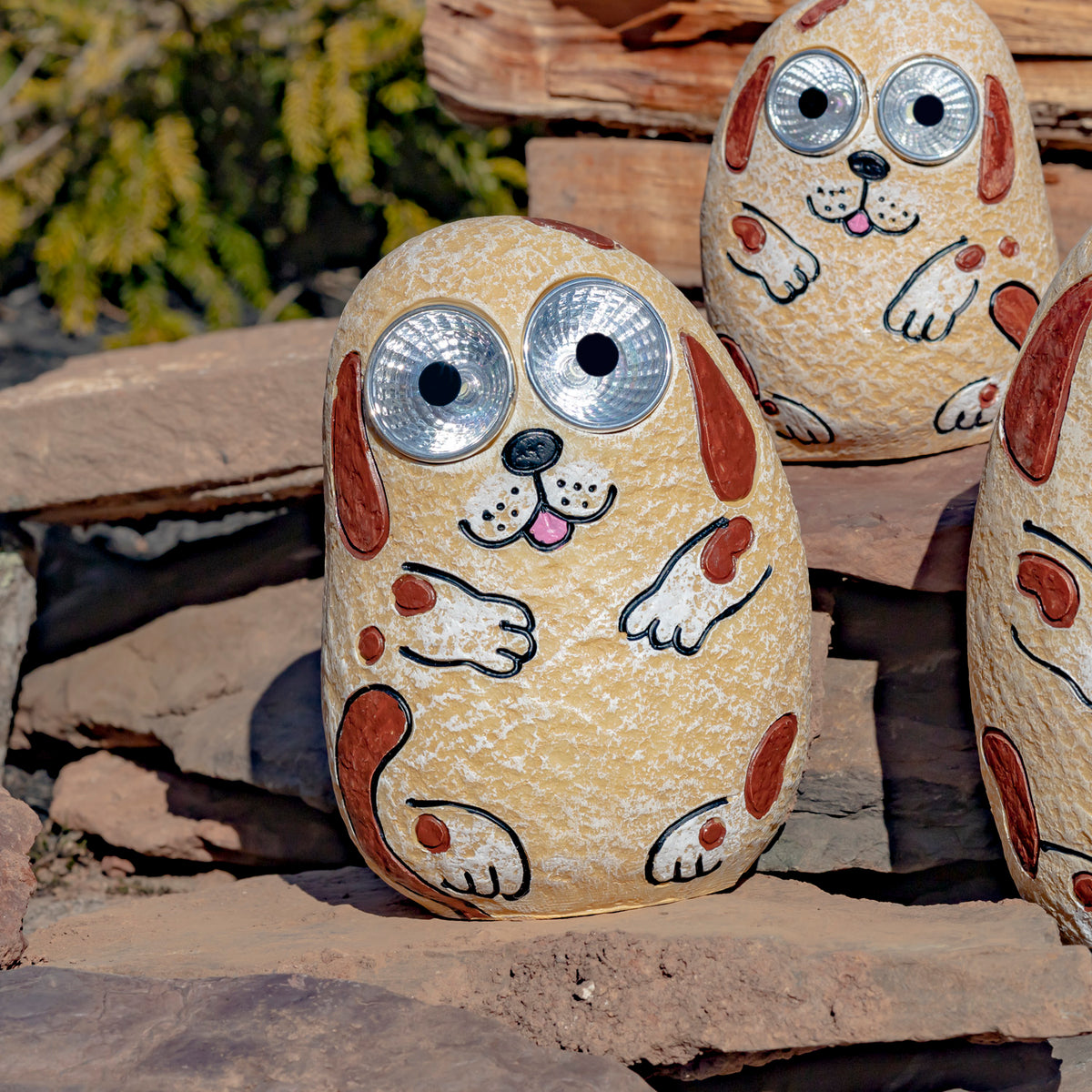A tan pebble-shaped dog ornament with brown markings and large silver eyes sits on a stone ledge.