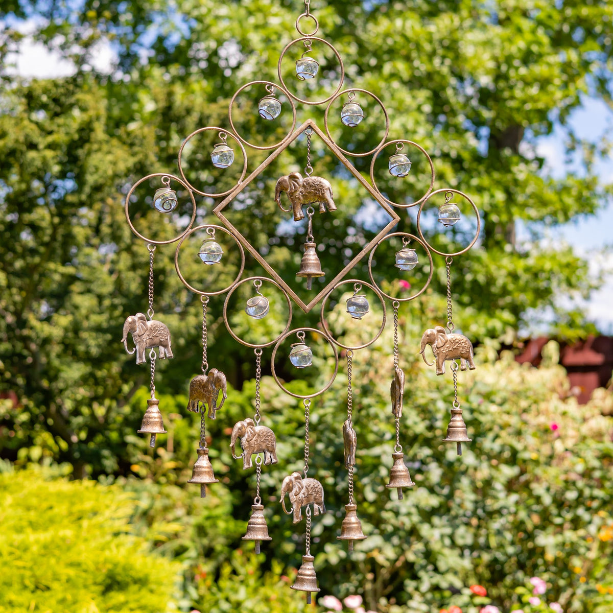 Metal wind chime with circular wirework, dangling elephant accents, and small bells hanging in a garden.