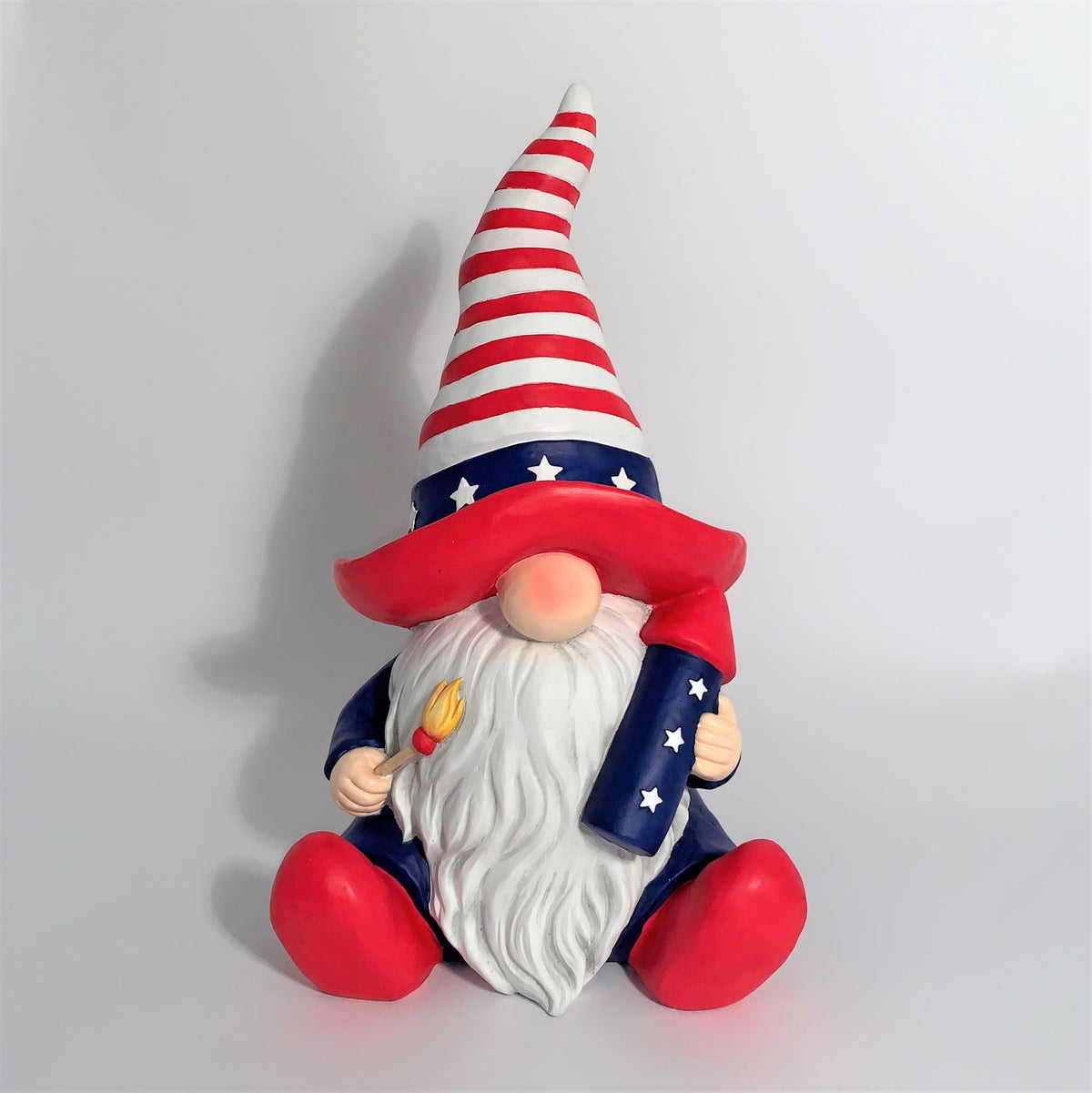 Front view of a seated red, white and blue garden gnome holding small objects