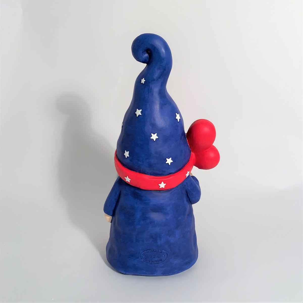 Back view of a blue garden gnome with red balloons and a curled hat