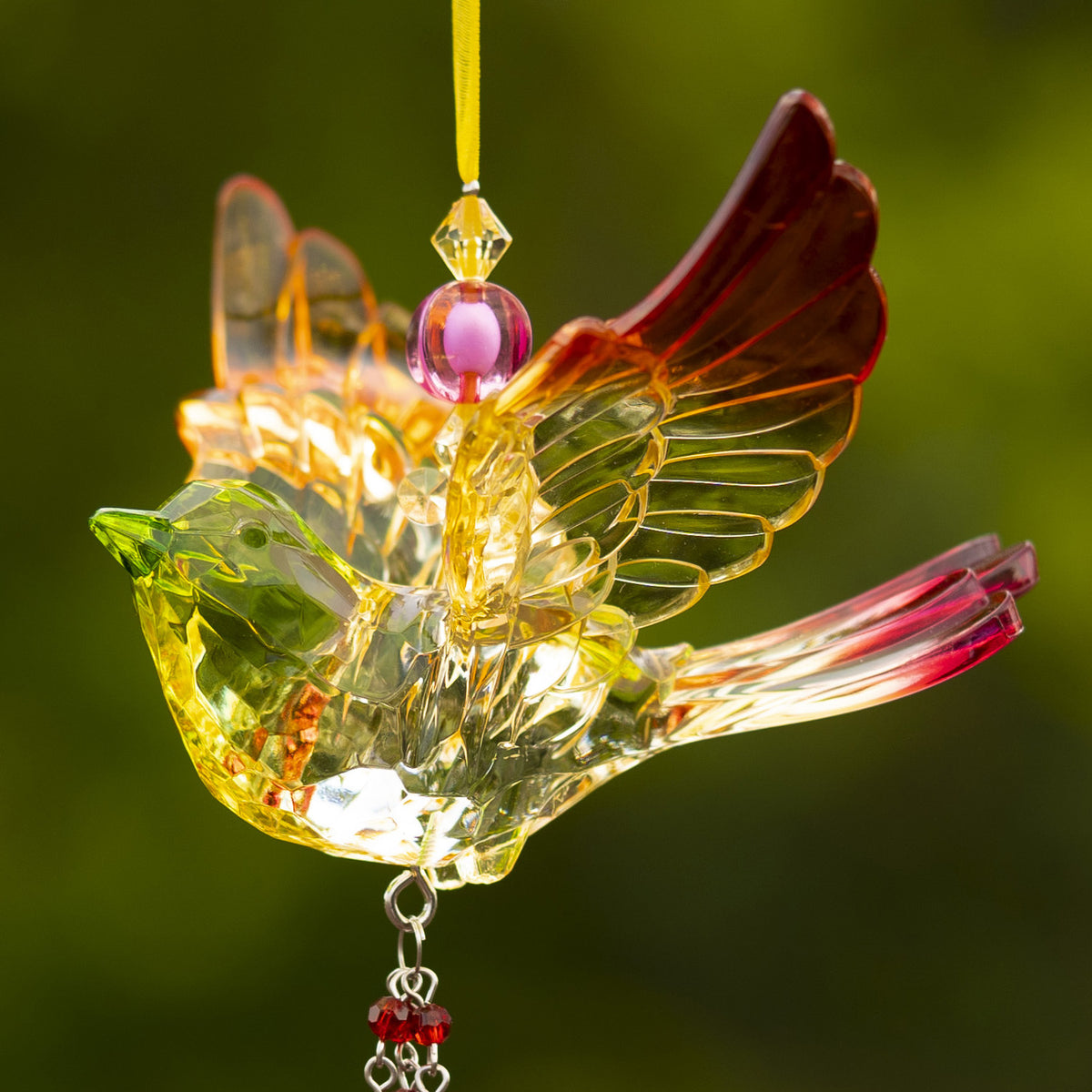 Close-up of a translucent multicolored bird ornament with raised wings and a beaded hanging strand.