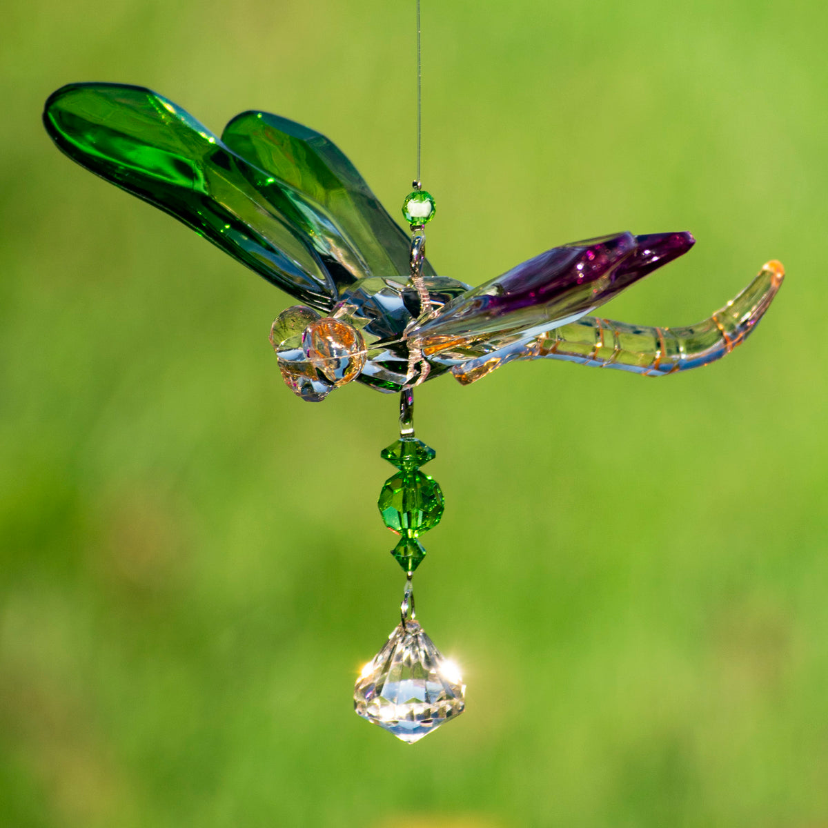 Green and purple acrylic dragonfly ornament with dangling green beads and a clear faceted drop against a blurred green