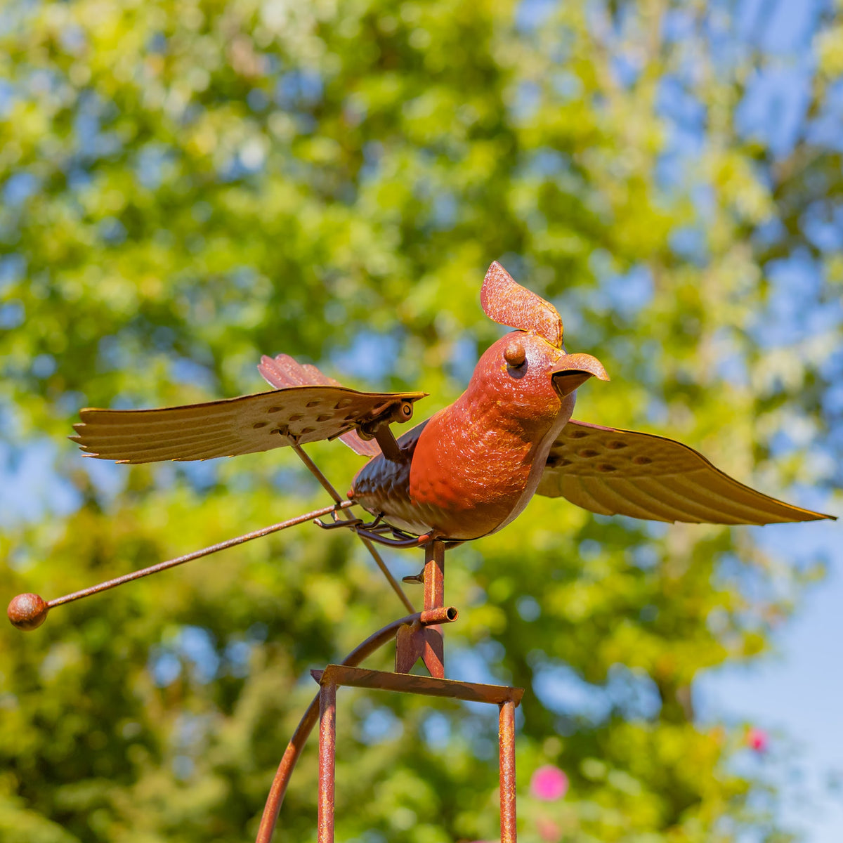 Closer view of the metal bird’s crest, beak, spread wings, and rocking mechanism against leafy greenery.