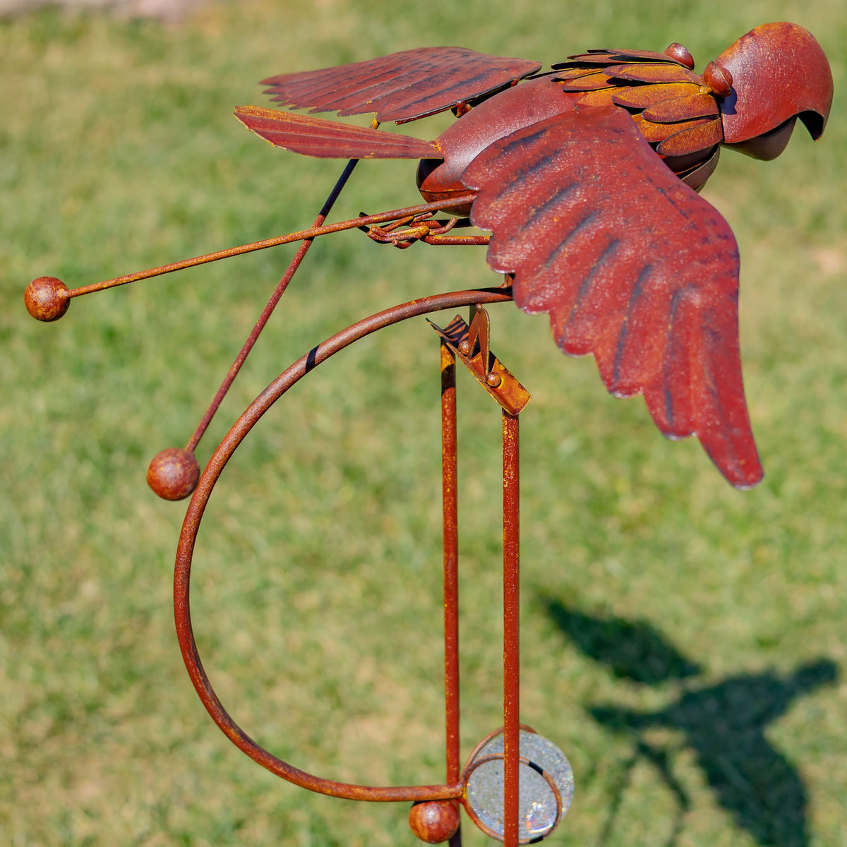 Close side view of the rust-colored bird ornament, curved rocking frame, and long metal stake against a lawn.
