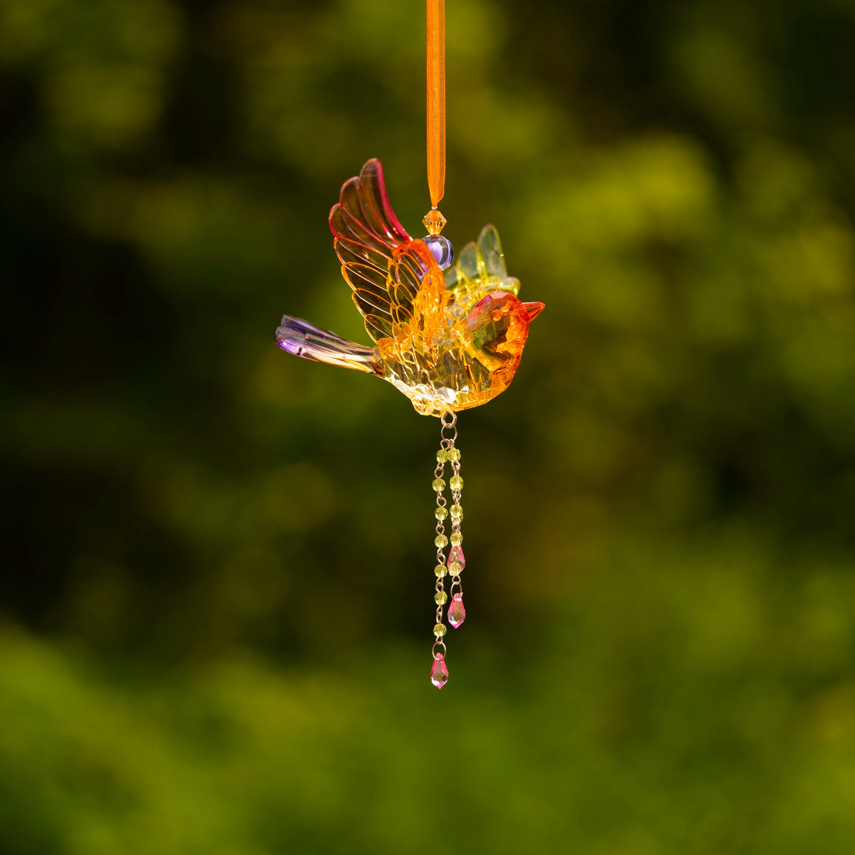 Amber-toned acrylic bird ornament hanging by an orange ribbon, with a raised wing and dangling beads.