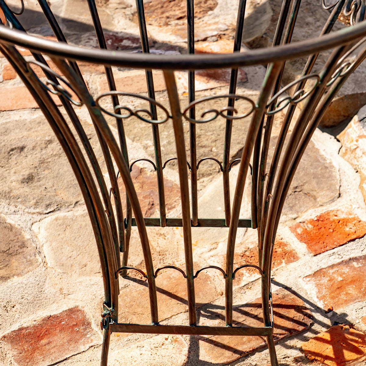 Close-up of the stand’s curved iron bars, scrollwork, and square base on a stone path.